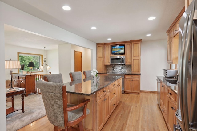 kitchen with recessed lighting, backsplash, appliances with stainless steel finishes, light wood-type flooring, and a kitchen breakfast bar