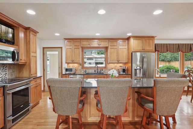 kitchen featuring a center island, light wood finished floors, backsplash, appliances with stainless steel finishes, and a sink