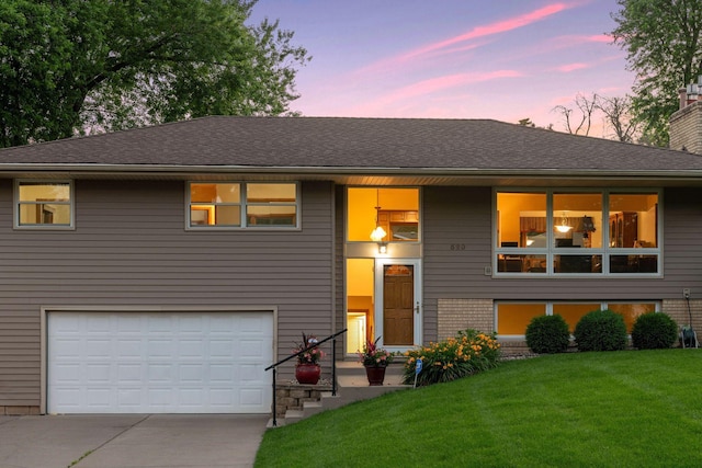 split foyer home with driveway, a lawn, a chimney, roof with shingles, and an attached garage