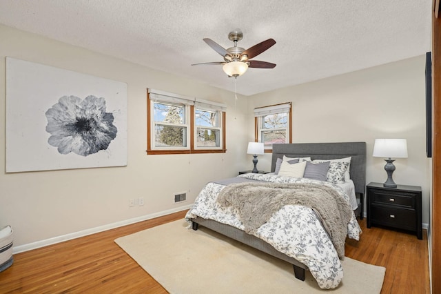 bedroom with visible vents, ceiling fan, baseboards, wood finished floors, and a textured ceiling