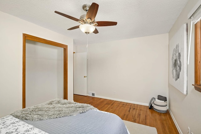 bedroom with visible vents, baseboards, wood finished floors, a closet, and a textured ceiling