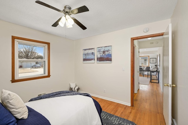 bedroom featuring ceiling fan, light wood-style floors, baseboards, and a textured ceiling