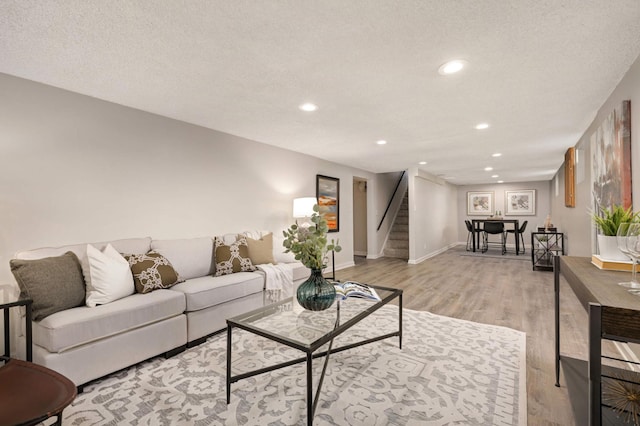 living area with light wood-style flooring, a textured ceiling, recessed lighting, baseboards, and stairs