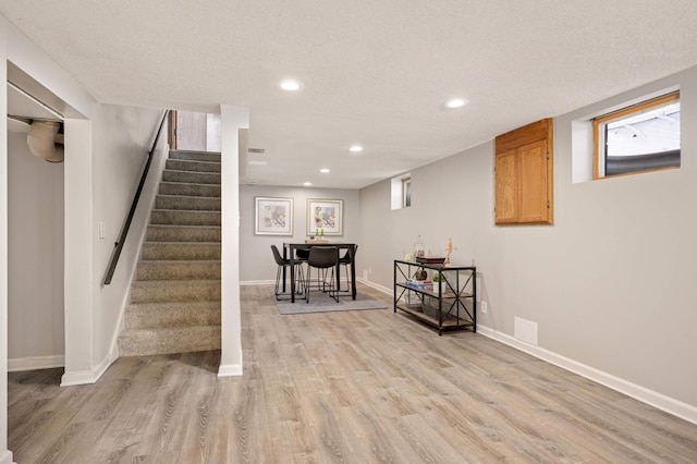 basement featuring baseboards, stairway, light wood-type flooring, recessed lighting, and a textured ceiling