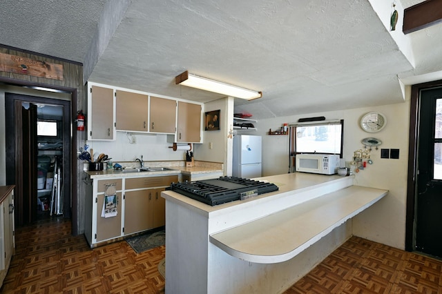 kitchen featuring light countertops, a sink, a textured ceiling, white appliances, and a peninsula