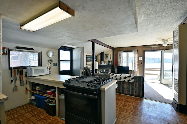 kitchen featuring black gas range, a ceiling fan, white microwave, open floor plan, and a textured ceiling