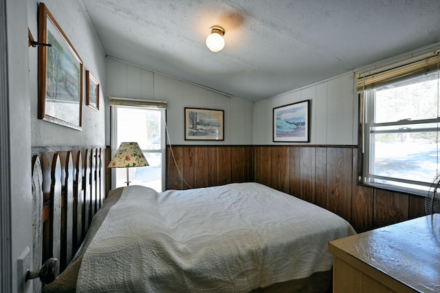 bedroom with lofted ceiling, wooden walls, and a textured ceiling