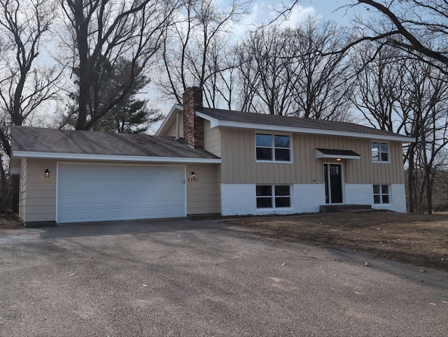 raised ranch with aphalt driveway, brick siding, an attached garage, and a chimney