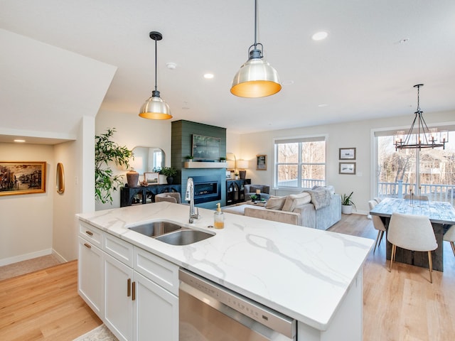 kitchen featuring open floor plan, stainless steel dishwasher, a sink, and light wood-style floors