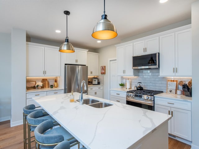 kitchen featuring stainless steel appliances, hanging light fixtures, a kitchen island with sink, a sink, and white cabinetry