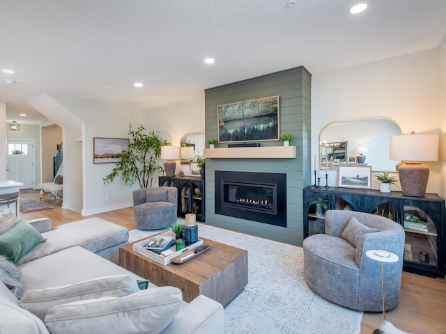 living area with a fireplace, recessed lighting, a textured ceiling, wood finished floors, and baseboards