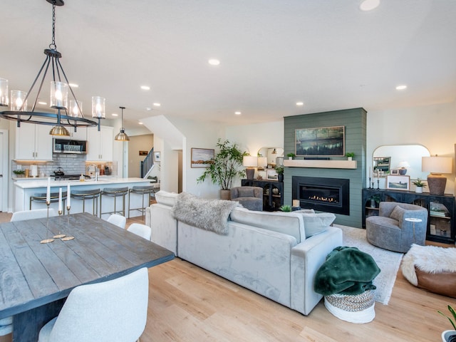 living room featuring recessed lighting, stairway, an inviting chandelier, a large fireplace, and light wood-type flooring