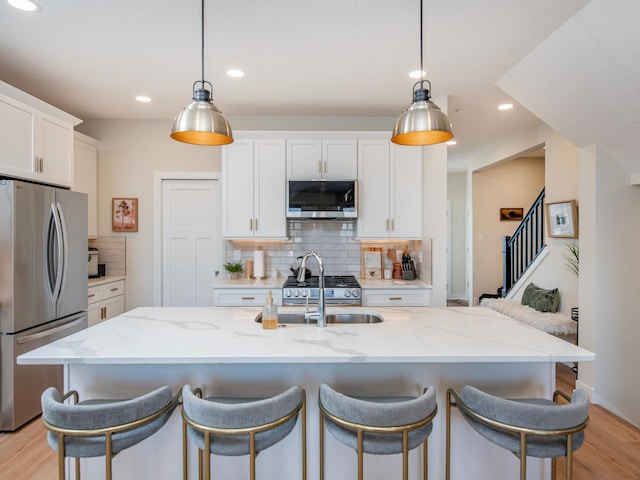 kitchen featuring a sink, white cabinetry, appliances with stainless steel finishes, light wood-type flooring, and tasteful backsplash