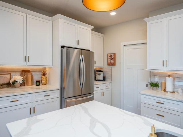 kitchen featuring tasteful backsplash, freestanding refrigerator, light stone countertops, white cabinetry, and recessed lighting