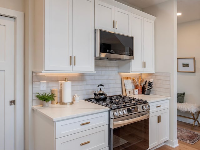 kitchen featuring appliances with stainless steel finishes, light stone counters, light wood-style floors, white cabinetry, and backsplash