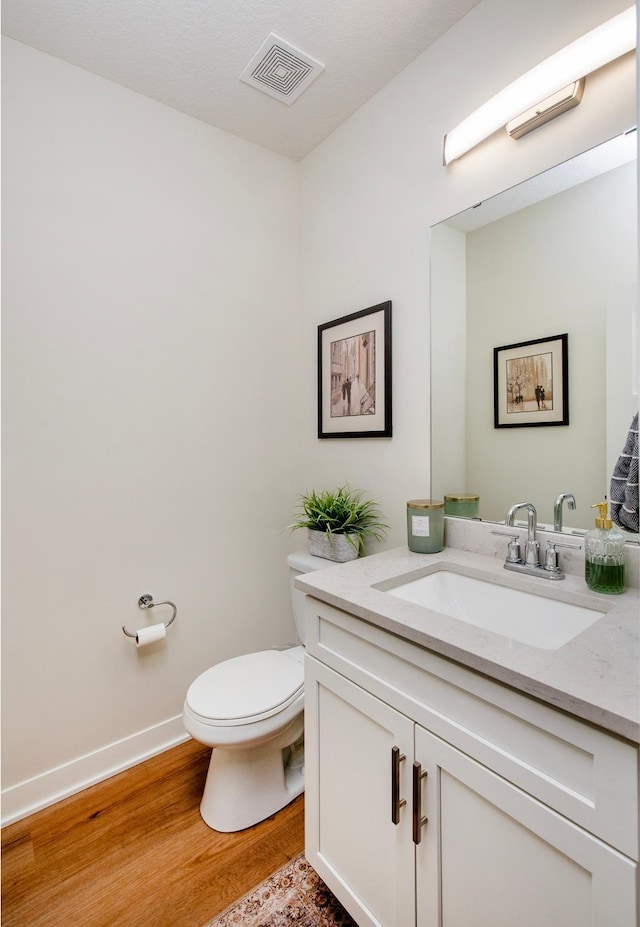 bathroom featuring toilet, wood finished floors, vanity, visible vents, and baseboards