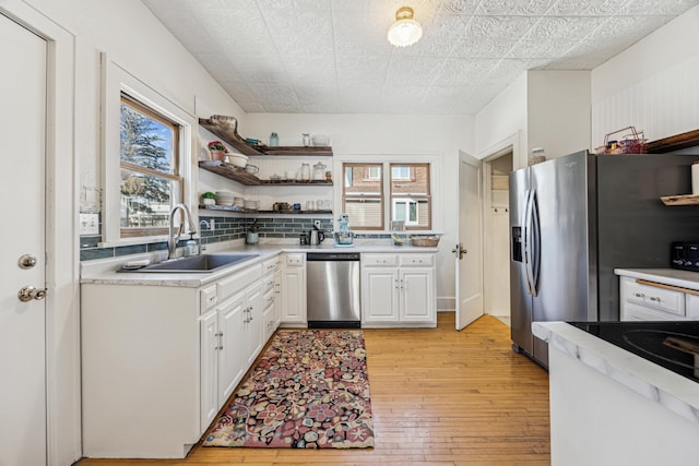 kitchen with a sink, tasteful backsplash, stainless steel appliances, light wood-style floors, and white cabinets