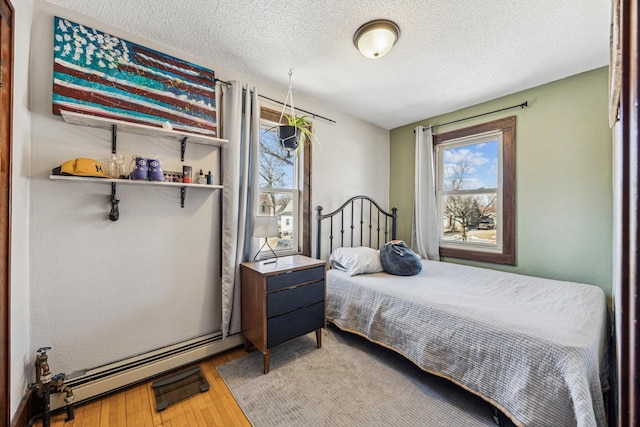 bedroom with a baseboard heating unit, light wood-type flooring, and a textured ceiling