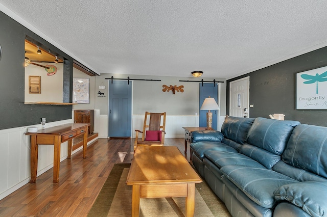 living room with a wainscoted wall, a barn door, a textured ceiling, and wood finished floors