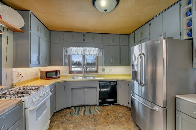 kitchen featuring black dishwasher, stainless steel refrigerator with ice dispenser, white gas range, gray cabinets, and a sink