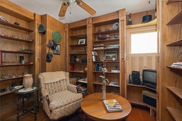 sitting room featuring wood walls, ceiling fan, and wood finished floors