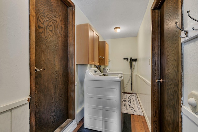 laundry room featuring a wainscoted wall, wood finished floors, washing machine and clothes dryer, and cabinet space