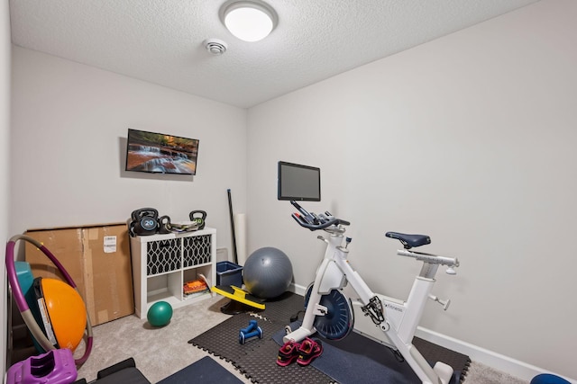 workout area featuring a textured ceiling, carpet flooring, and baseboards