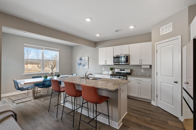 kitchen featuring dark wood-style flooring, a sink, visible vents, appliances with stainless steel finishes, and a center island with sink