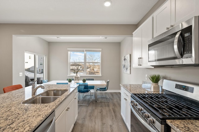 kitchen with appliances with stainless steel finishes, a sink, white cabinetry, and light wood-style floors