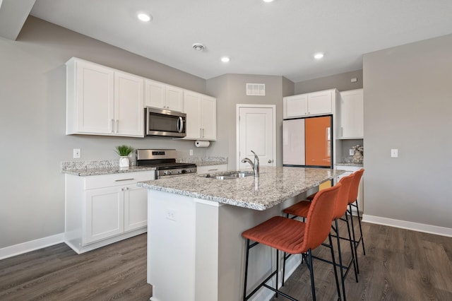 kitchen with light stone counters, stainless steel appliances, a breakfast bar, a sink, and visible vents