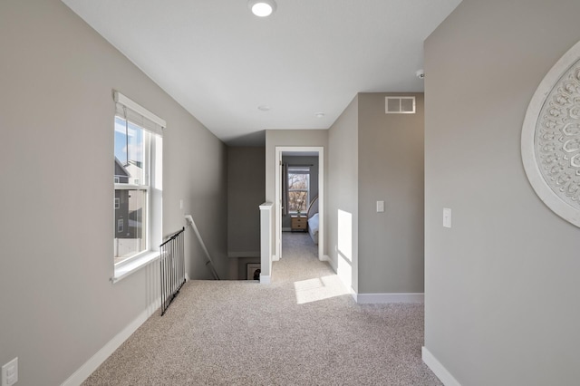 hallway featuring visible vents, carpet flooring, a wealth of natural light, and an upstairs landing