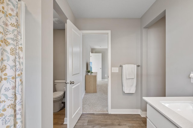 bathroom featuring toilet, baseboards, wood finished floors, and vanity