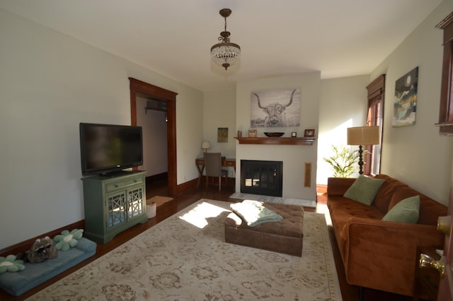 living area with a fireplace with flush hearth, a chandelier, baseboards, and wood finished floors