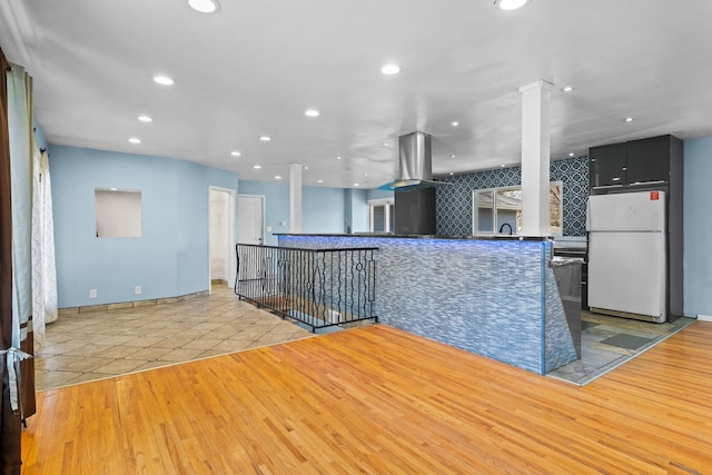 kitchen with light wood-style floors, freestanding refrigerator, dark cabinets, a peninsula, and ornate columns