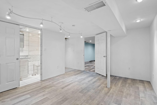 finished basement with light wood-type flooring, visible vents, and track lighting