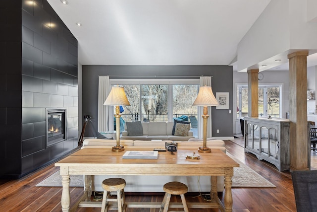 home office featuring a large fireplace, baseboards, wood finished floors, and ornate columns