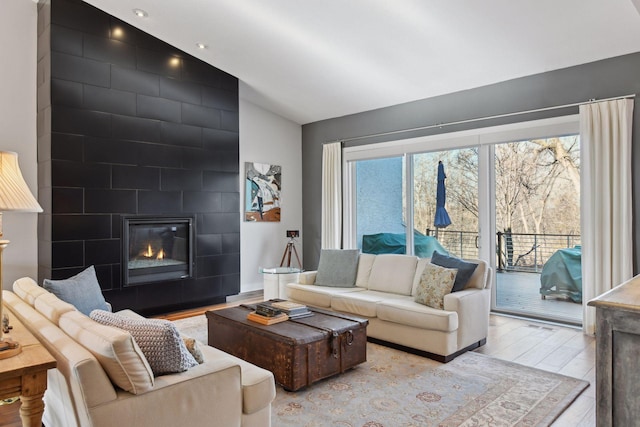 living room featuring a large fireplace, vaulted ceiling, and wood finished floors