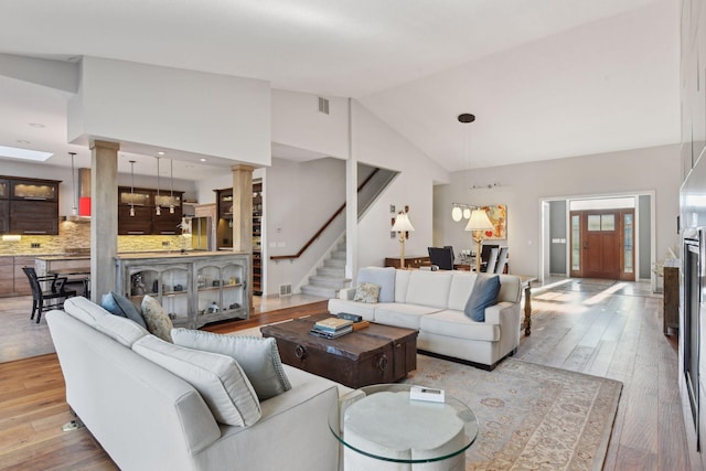 living room with lofted ceiling, visible vents, light wood-style flooring, stairway, and ornate columns