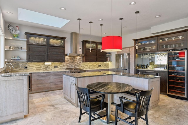 kitchen with wine cooler, a skylight, freestanding refrigerator, wall chimney exhaust hood, and an island with sink