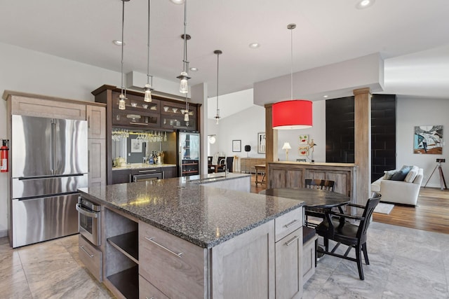 kitchen with glass insert cabinets, recessed lighting, decorative light fixtures, appliances with stainless steel finishes, and a center island with sink