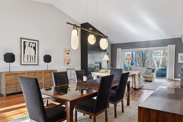 dining space with high vaulted ceiling, a large fireplace, and wood finished floors