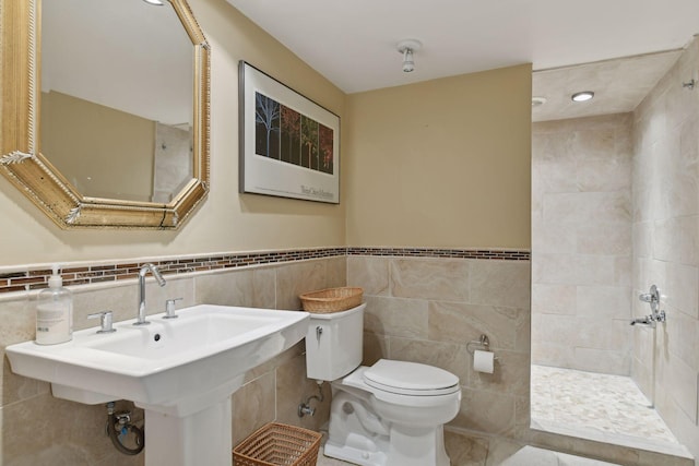 full bathroom featuring tile walls, tiled shower, wainscoting, toilet, and a sink