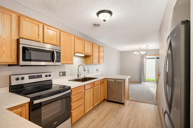 kitchen with light brown cabinets, a peninsula, a sink, light countertops, and appliances with stainless steel finishes