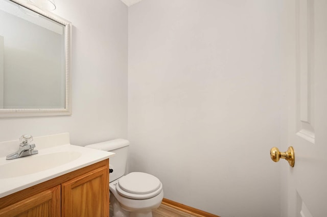 bathroom featuring toilet, baseboards, wood finished floors, and vanity