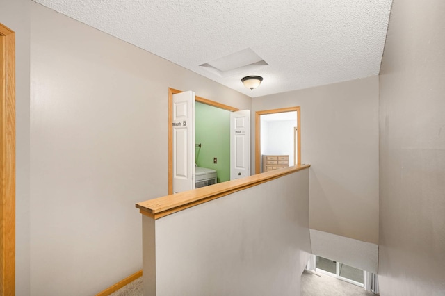 hall with washer / dryer, attic access, an upstairs landing, carpet flooring, and a textured ceiling