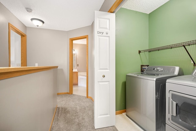 clothes washing area with washer and clothes dryer, light carpet, a textured ceiling, laundry area, and baseboards