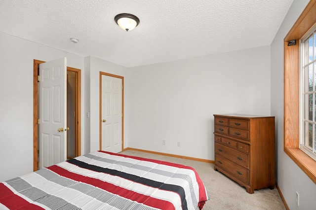 bedroom with light colored carpet, a textured ceiling, and baseboards