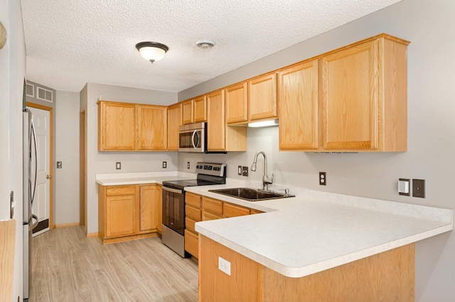 kitchen with stainless steel appliances, light countertops, a sink, light wood-type flooring, and a peninsula