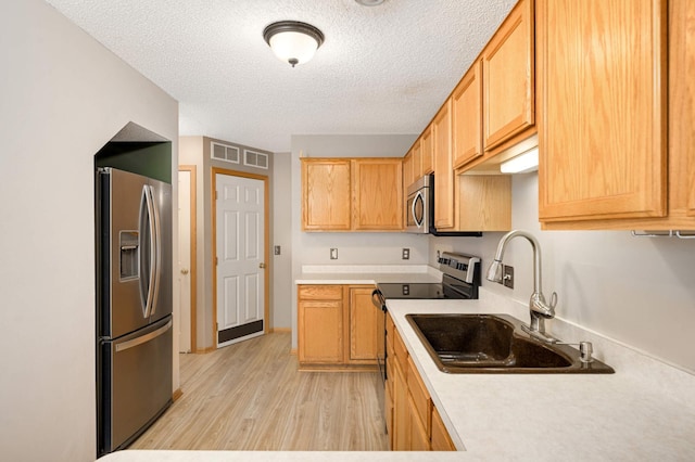 kitchen with stainless steel appliances, light countertops, a sink, a textured ceiling, and light wood-type flooring