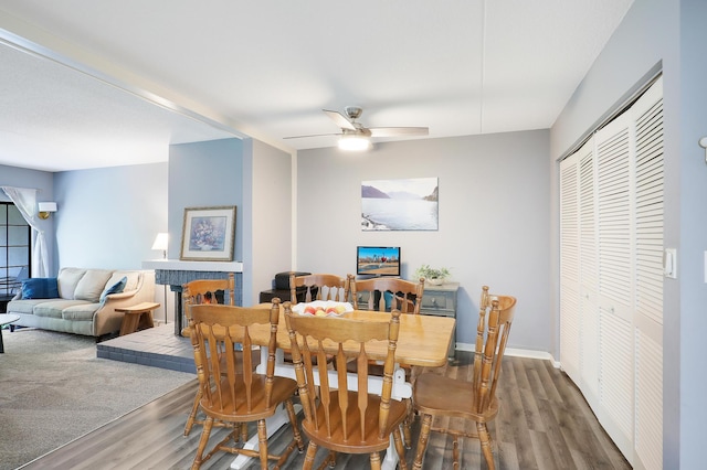 dining space featuring dark wood-style flooring, a brick fireplace, a ceiling fan, and baseboards